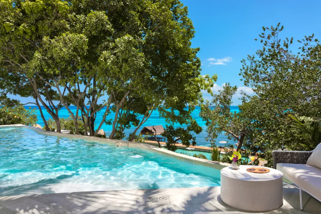 Elevated infinity pool surrounded by tropical trees with ocean view at Impression Isla Mujeres by Secrets.