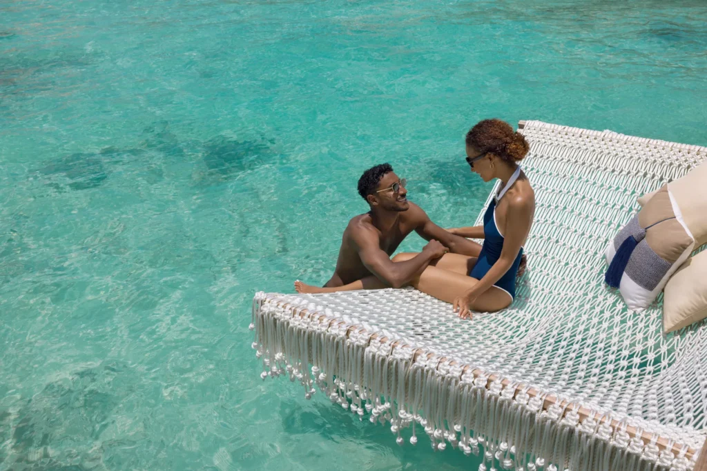 Couple relaxing on an overwater hammock above crystal-clear turquoise water at Impression Isla Mujeres by Secrets.