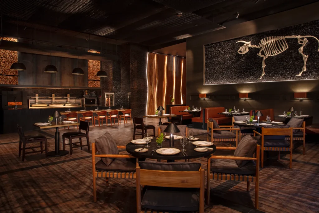 Ember steakhouse at Impression Moxché by Secrets featuring a moody fire-grill dining room, open kitchen, and upscale steakhouse ambiance.