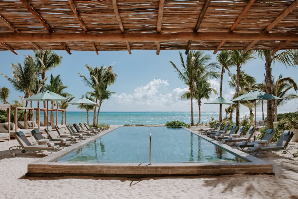 Oceanfront beach club pool with palm trees and loungers at Impression Moxché by Secrets.