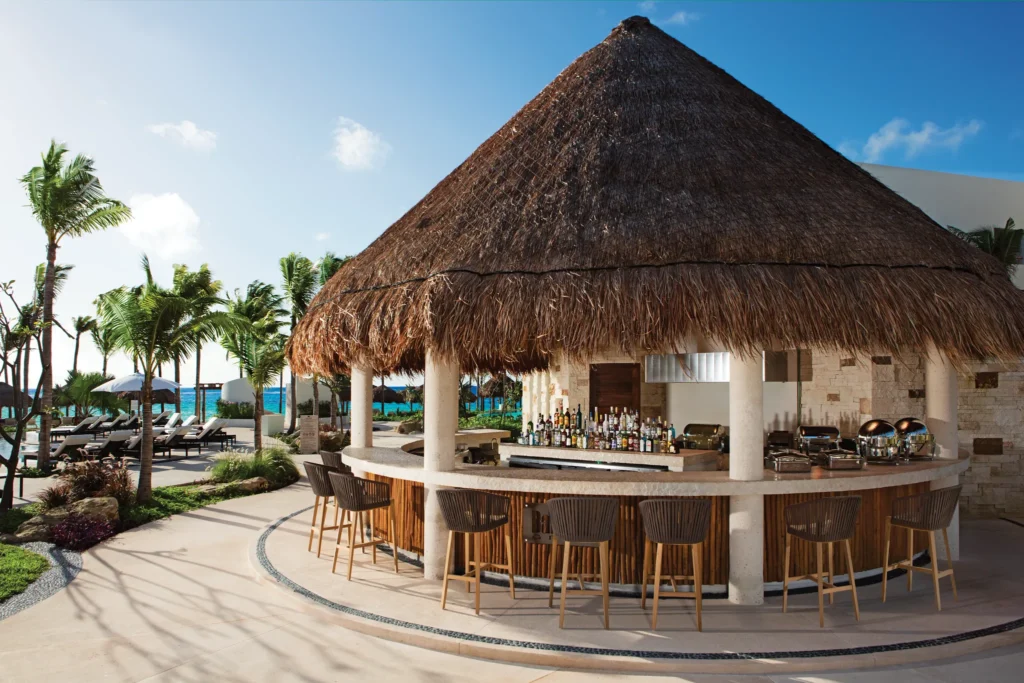 Barefoot Grill at Secrets Akumal Riviera Maya featuring a thatched-roof outdoor bar, casual lunch seating, and tropical resort surroundings near the beach.