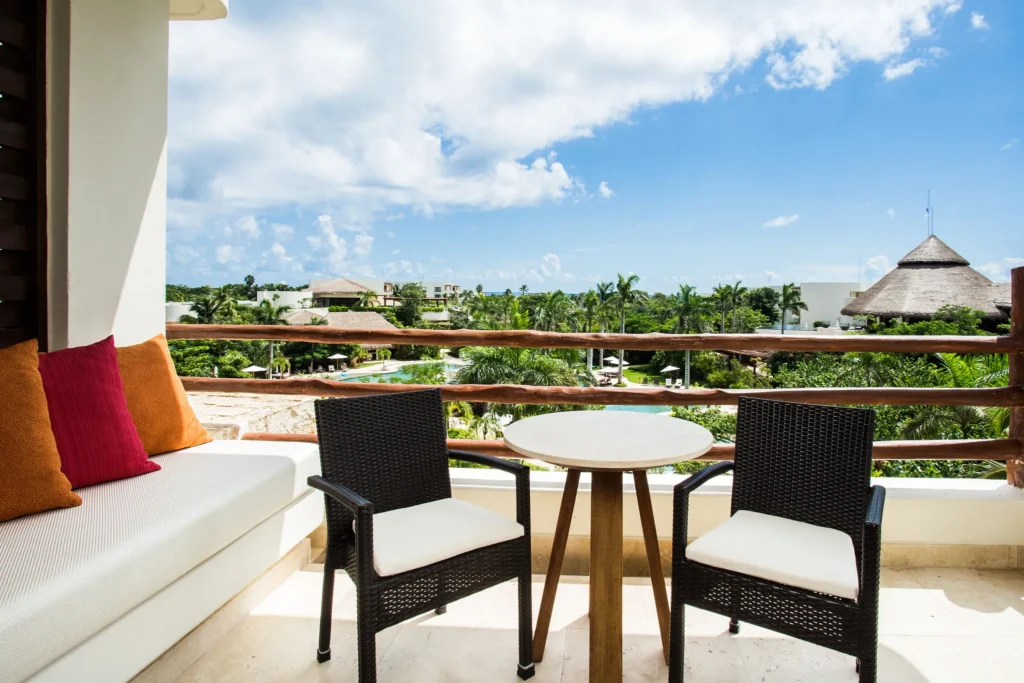 Junior Suite Partial Ocean View balcony with table and chairs at Secrets Akumal Riviera Maya overlooking tropical grounds.