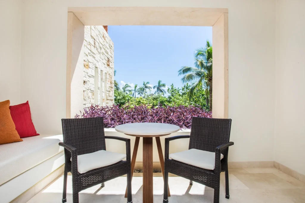 Junior Suite Tropical View furnished terrace with table and chairs at Secrets Akumal Riviera Maya overlooking lush greenery.
