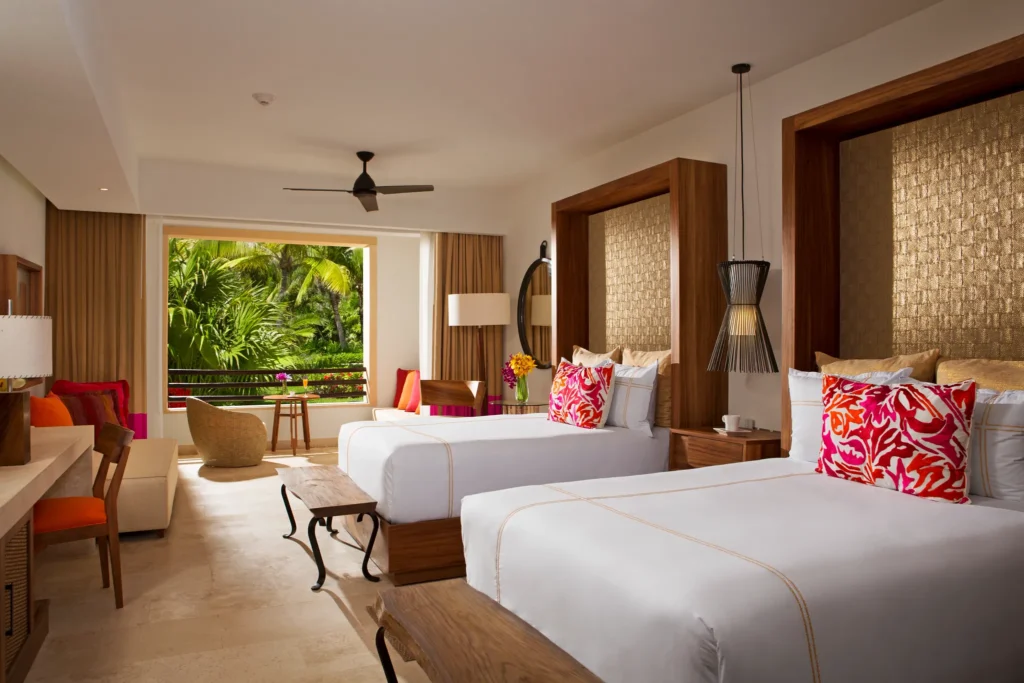 Junior Suite Tropical View with two double beds and sitting area at Secrets Akumal Riviera Maya with tropical scenery outside.