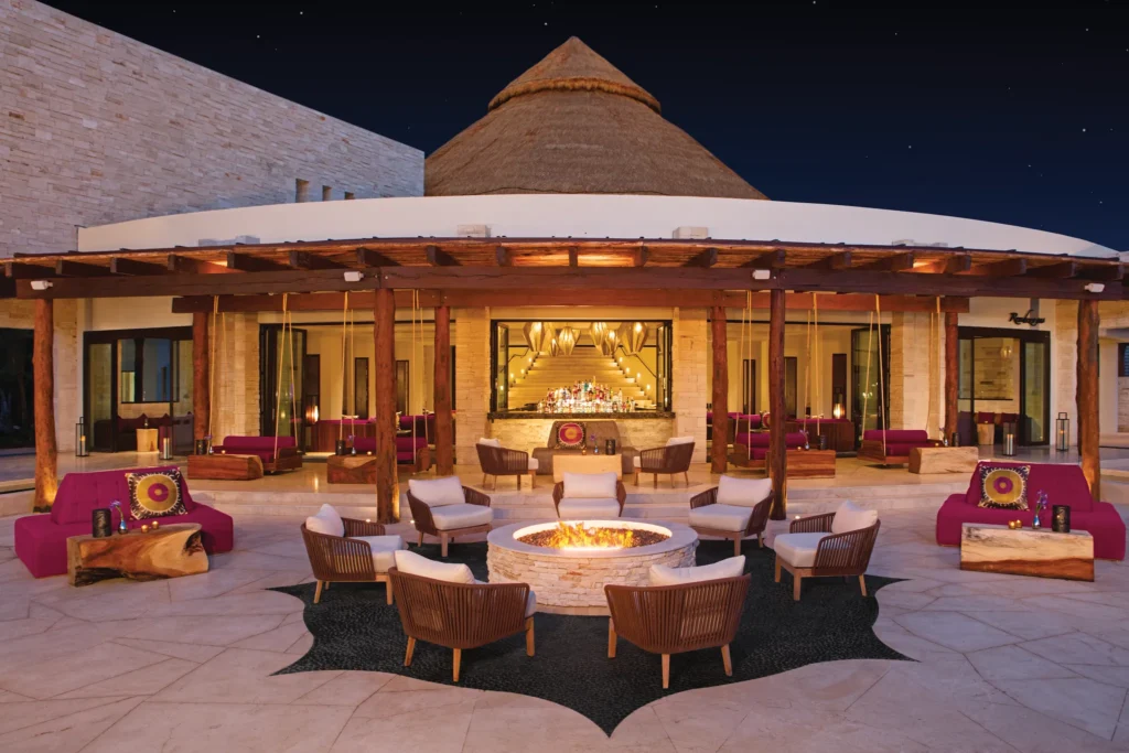 Rendezvous Lobby Bar at Secrets Akumal Riviera Maya featuring chic open-air lounge seating, a central fire pit, warm evening lighting, and handcrafted cocktails in a stylish resort setting.