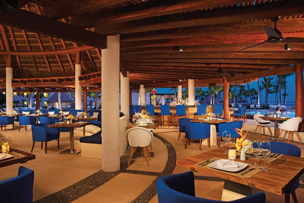 Seaside Grill at Secrets Akumal Riviera Maya featuring an open-air poolside restaurant with blue lounge chairs, tropical décor, and evening dining ambiance.