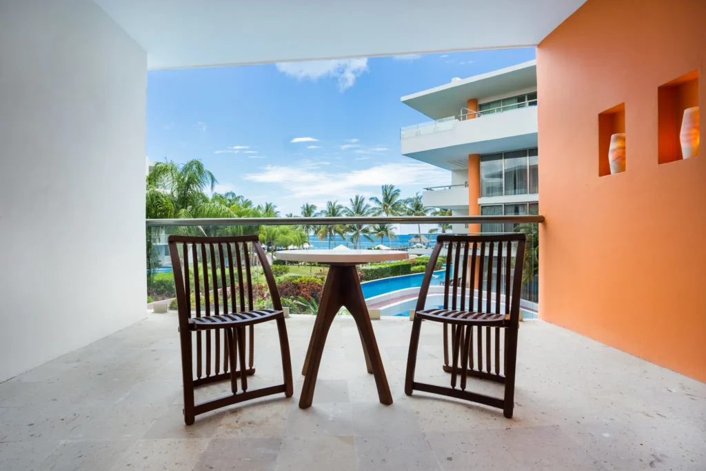 Private balcony with chairs and table overlooking ocean and pool at Secrets Aura Cozumel.
