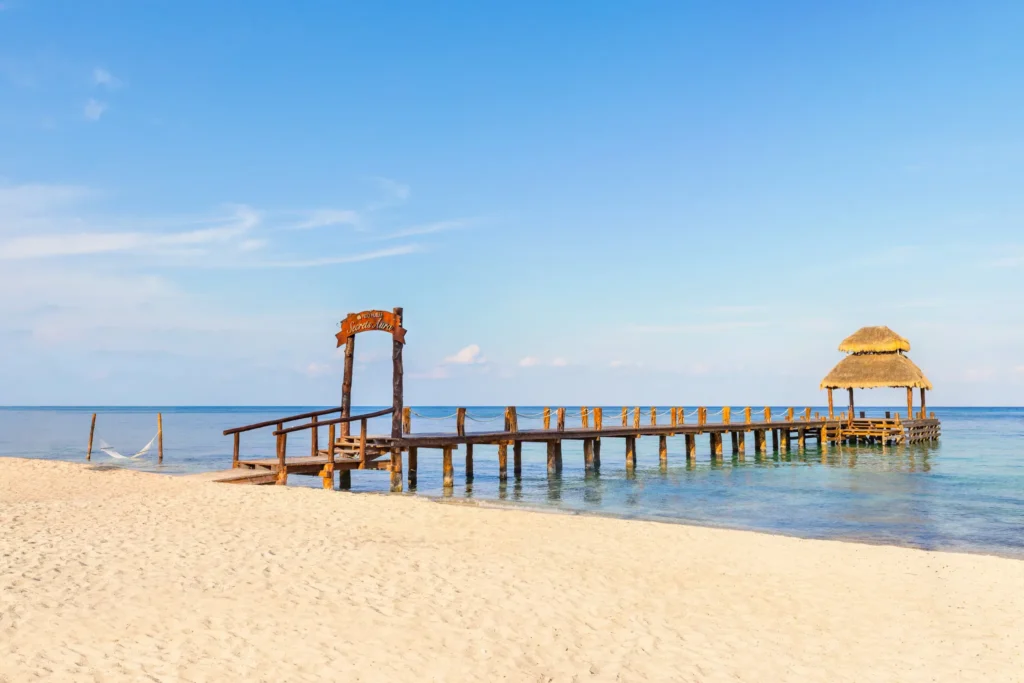 Wooden pier entrance on sandy beach at Secrets Aura Cozumel with turquoise Caribbean water.