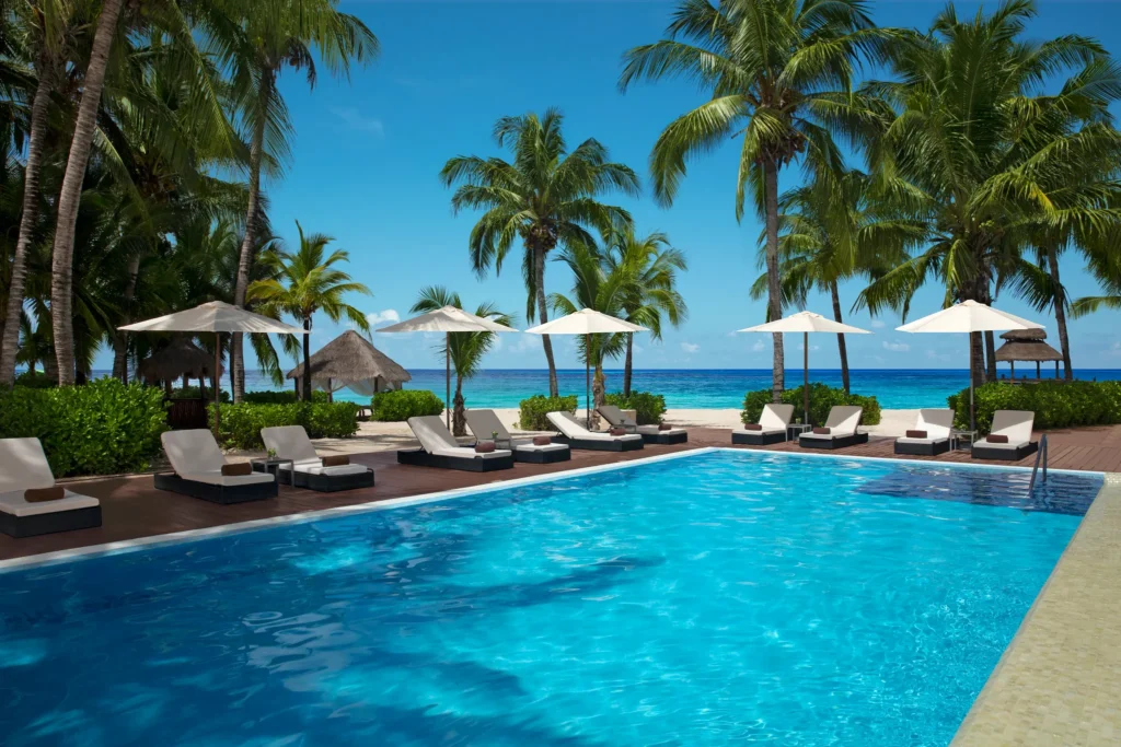Resort pool with lounge chairs and palm trees overlooking beach at Secrets Aura Cozumel.