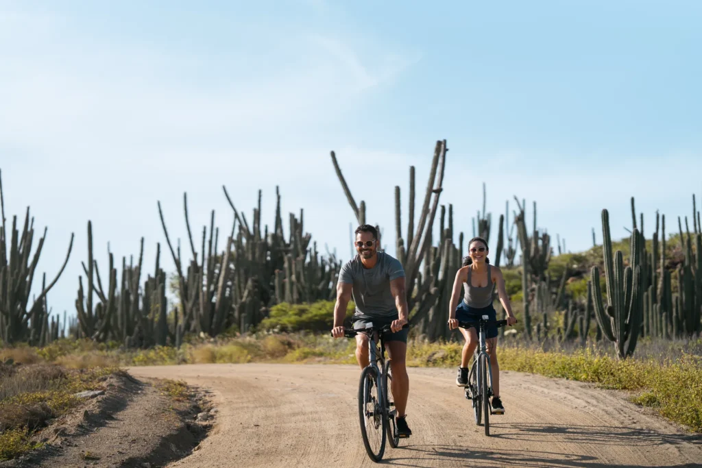 Active couple biking through Aruba’s desert landscape near Secrets Baby Beach Aruba resort.