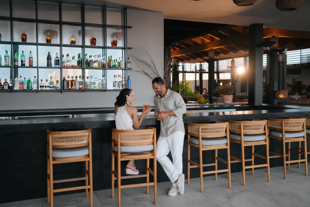Couple sharing cocktails at a stylish resort bar inside Secrets Baby Beach Aruba.