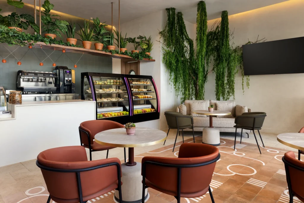 Coco Café at Secrets Baby Beach Aruba featuring a modern coffee bar, pastry display case, and cozy indoor seating with lush greenery décor.