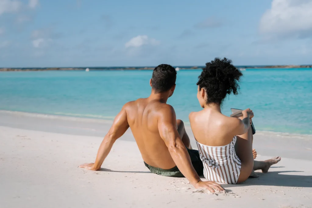 Couple sitting on the white-sand shores of Baby Beach in Aruba, enjoying crystal-clear turquoise waters near Secrets Baby Beach Aruba. Couple sitting on the white-sand shores of Baby Beach in Aruba, enjoying crystal-clear turquoise waters near Secrets Baby Beach Aruba.