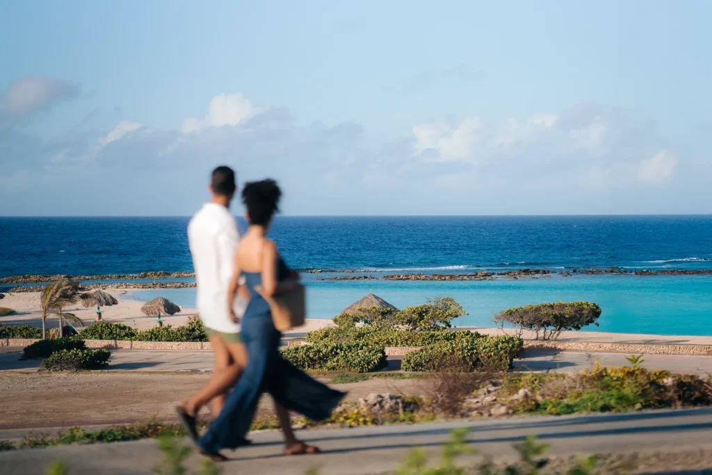 Couple strolling along the scenic coastline near Secrets Baby Beach Aruba with turquoise Caribbean waters in the background.
