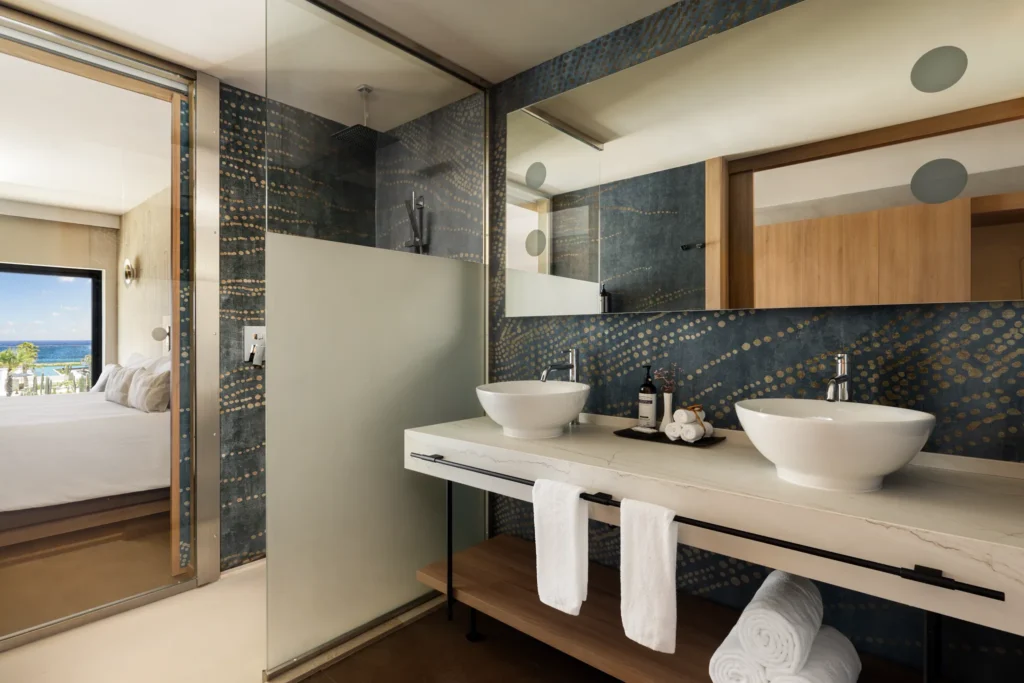 Junior Suite bathroom with dual vessel sinks and glass-enclosed rain shower at Secrets Baby Beach Aruba.