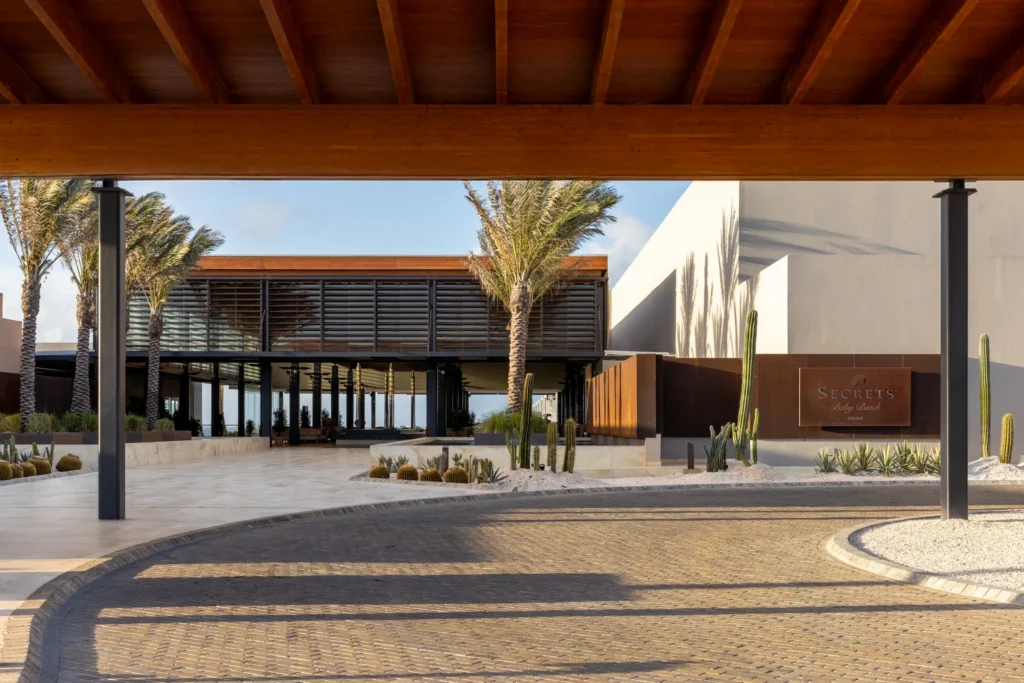 Modern entrance and motor lobby at Secrets Baby Beach Aruba with palm trees and desert landscaping.