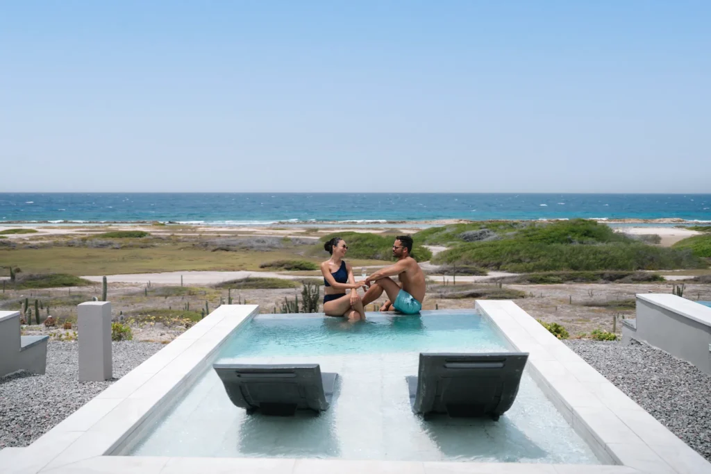 Couple relaxing in a tranquil pool surrounded by palm trees at Secrets Baby Beach Aruba.