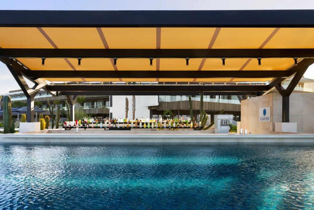 Sugar Reef Pool Bar at Secrets Baby Beach Aruba featuring a swim-up bar, tropical cocktails, and modern open-air poolside setting.