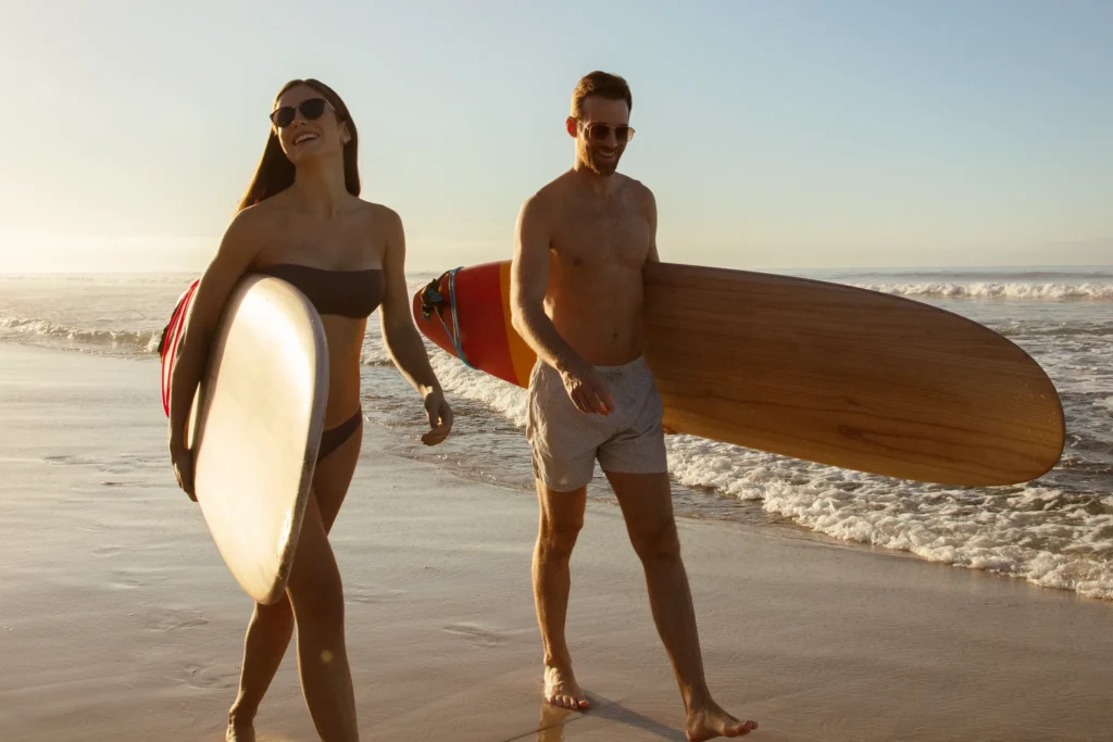 Smiling couple walking along the shoreline with surfboards at Secrets Bahia Mita Surf & Spa Resort, enjoying a surf-inspired adults-only getaway.