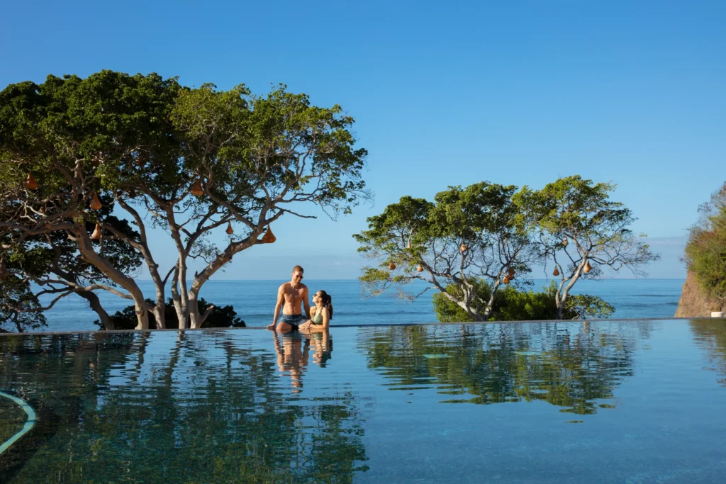 Couple relaxing together in an infinity pool with ocean views at Secrets Bahia Mita Surf & Spa Resort.