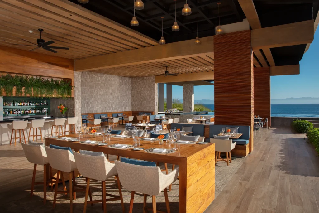 Seaside Grill at Secrets Bahia Mita Surf & Spa Resort featuring open-air poolside dining with ocean views, wooden tables, and casual resort ambiance.