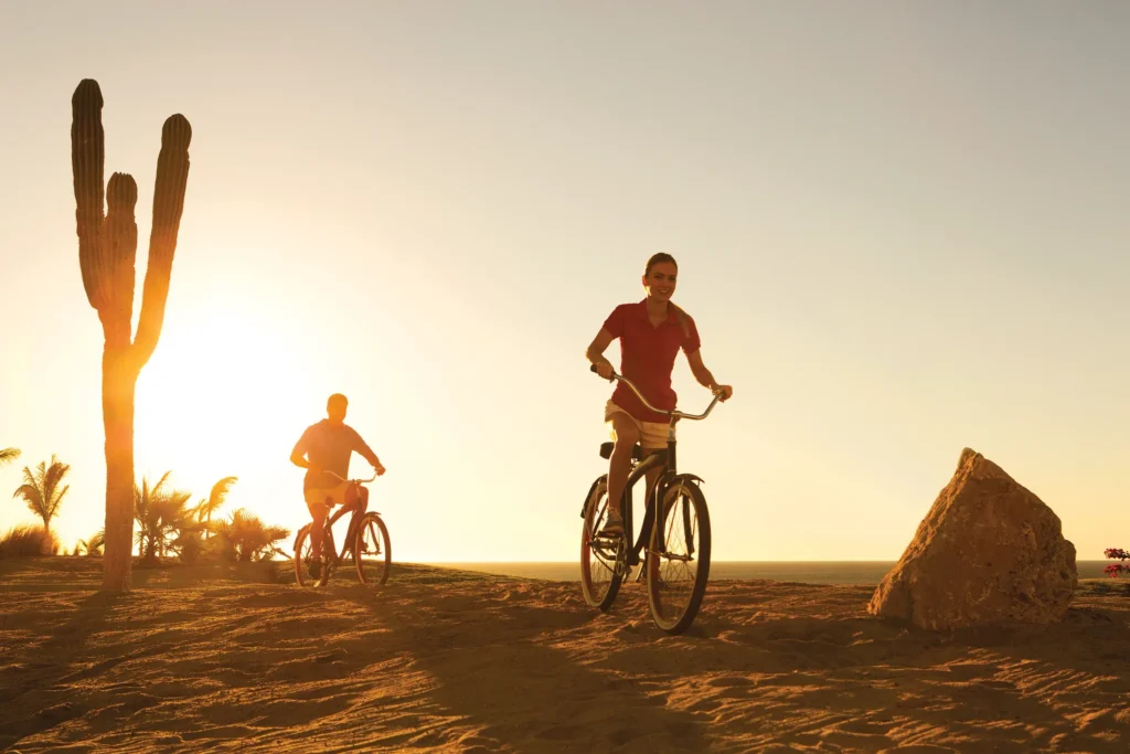 Couple riding bicycles along the beach at sunset near Secrets Puerto Los Cabos Golf & Spa Resort.