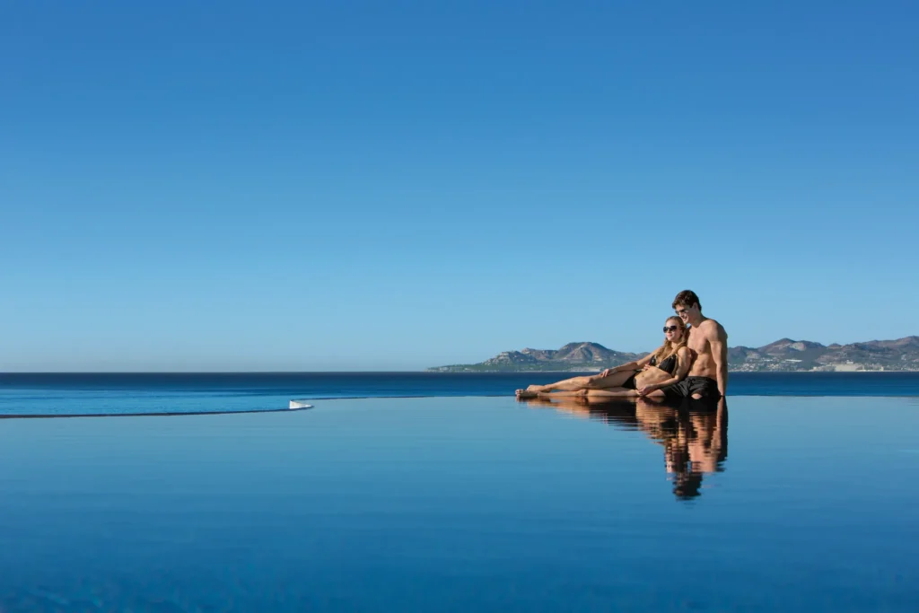 Couple relaxing in an infinity pool overlooking the Sea of Cortez at Secrets Puerto Los Cabos.