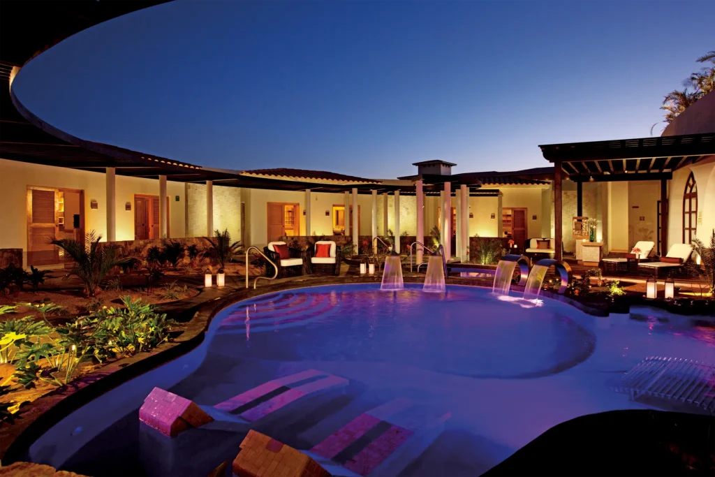 Illuminated spa pool with water features at night at Secrets Puerto Los Cabos resort.