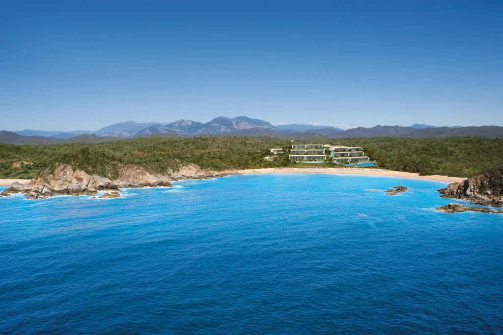 Aerial view of the secluded bay and beachfront at Secrets Huatulco Resort & Spa with mountains and turquoise waters.