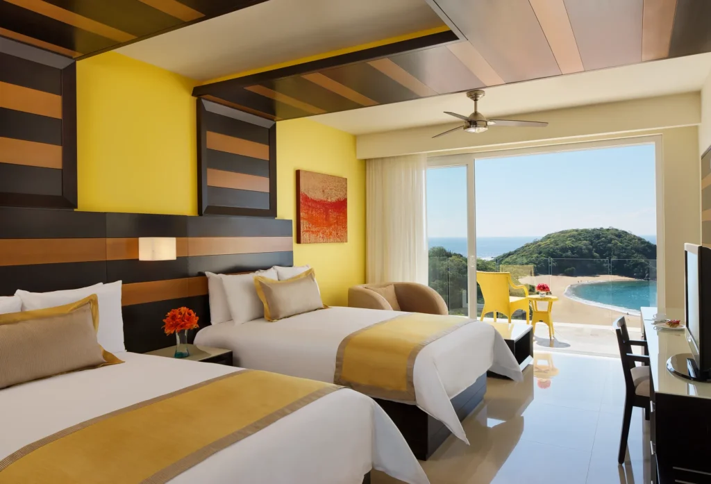 Junior Suite Ocean Front with two double beds and private balcony at Secrets Huatulco Resort & Spa overlooking the Pacific Ocean.