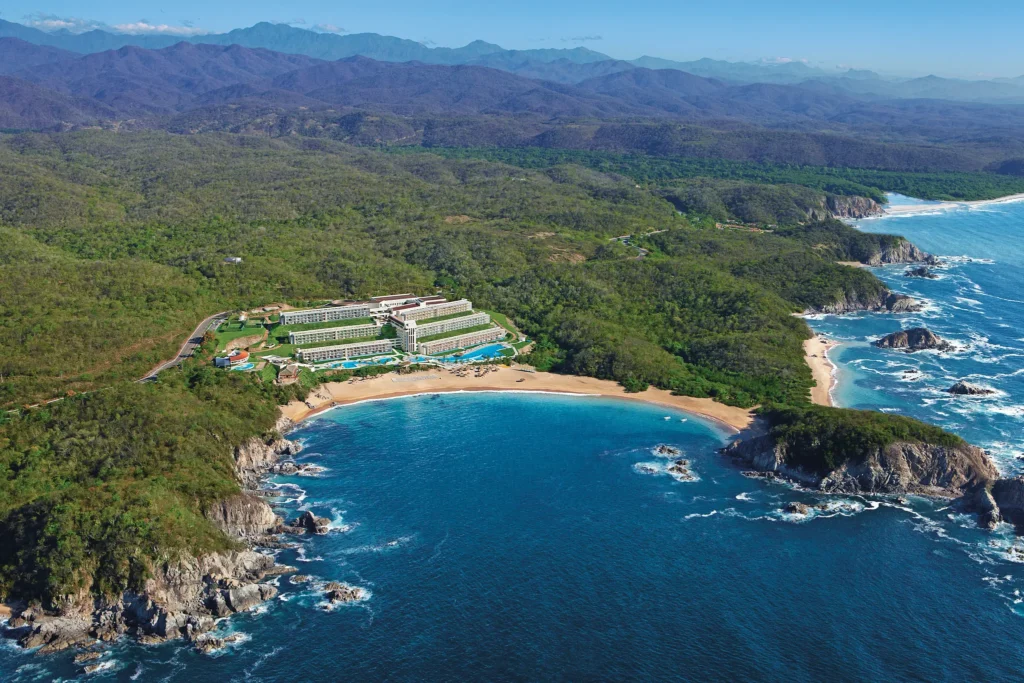 Aerial view of Secrets Huatulco Resort & Spa nestled between lush mountains and a secluded bay along the Pacific coast of Mexico.