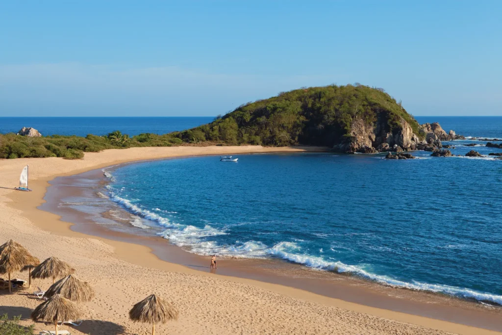 Panoramic view of Conejos Bay near Secrets Huatulco Resort & Spa, featuring golden sand, calm waters, and dramatic coastal scenery.