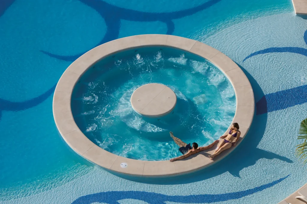 Couple relaxing in an outdoor whirlpool surrounded by turquoise pools at Secrets Huatulco Resort & Spa, an adults-only luxury escape.
