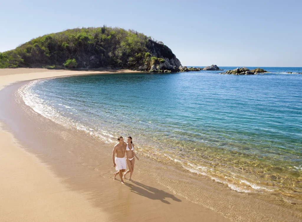 Couple walking hand-in-hand along the sandy beach at Secrets Huatulco Resort & Spa, perfect for romantic getaways.