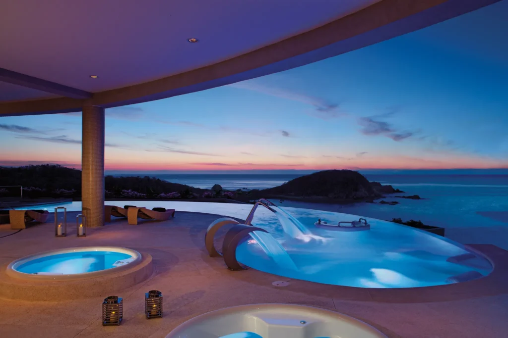 Illuminated spa circuit pools at night with ocean views at Secrets Huatulco Resort & Spa.
