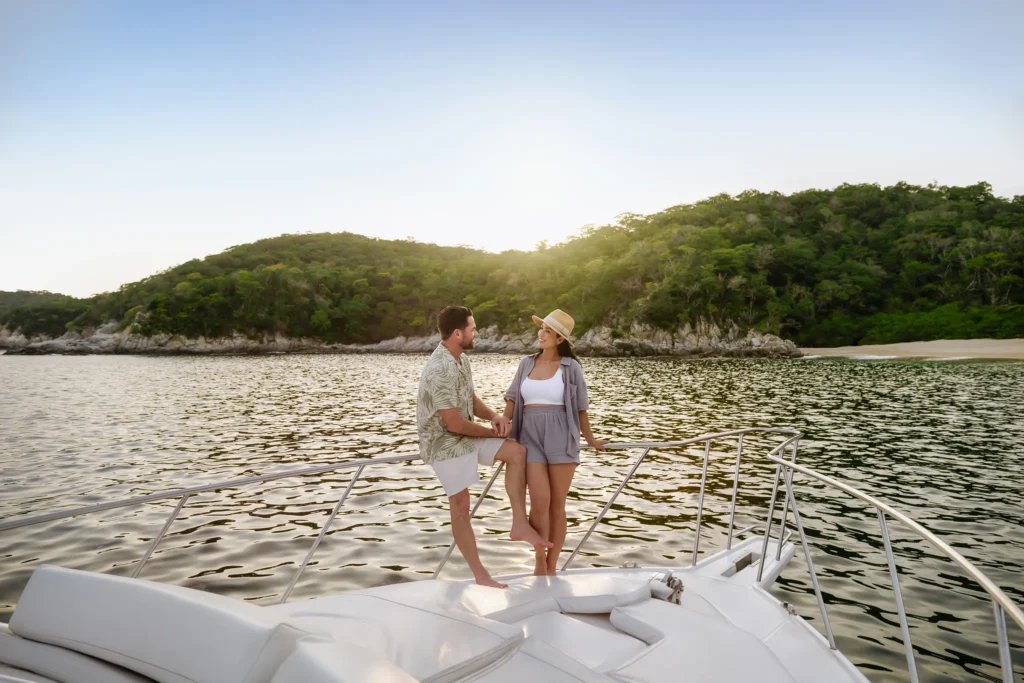 Couple relaxing on a luxury catamaran during sunset near Secrets Huatulco Resort & Spa, overlooking calm waters and forested coastline.