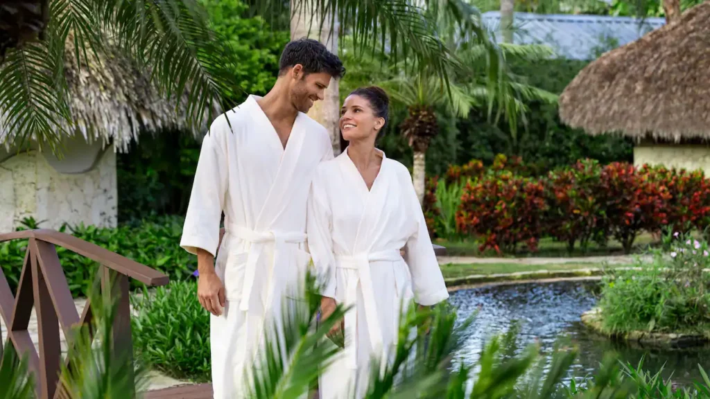 Couple in spa robes walking through tropical gardens at Secrets La Romana Resort & Spa.