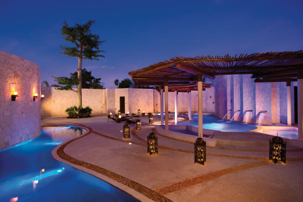 Outdoor hydrotherapy pools and spa circuit illuminated at night at Secrets Maroma Beach Riviera Cancun.