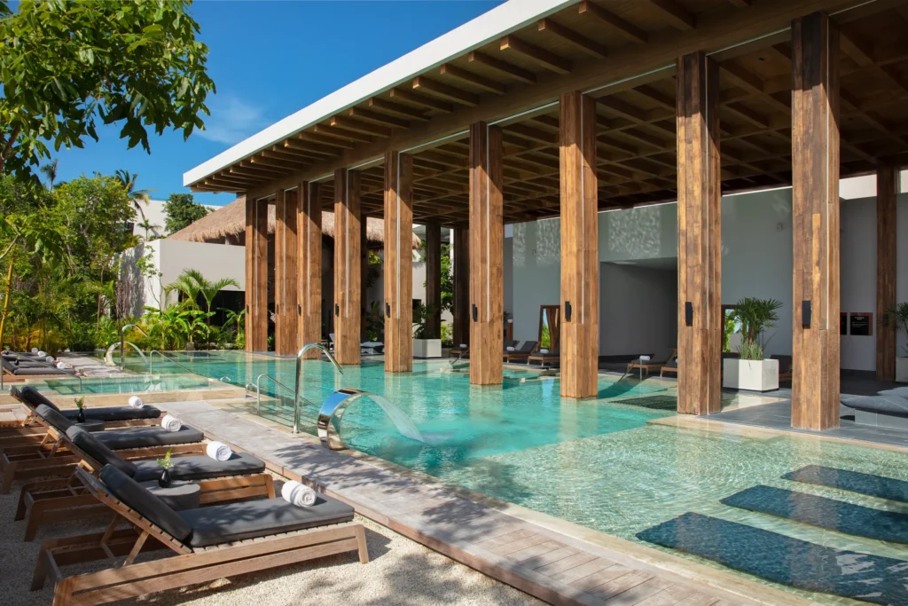 Outdoor hydrotherapy pool with lounge chairs and wooden columns at the Secrets Spa by Pevonia at Secrets Moxché Playa Del Carmen.