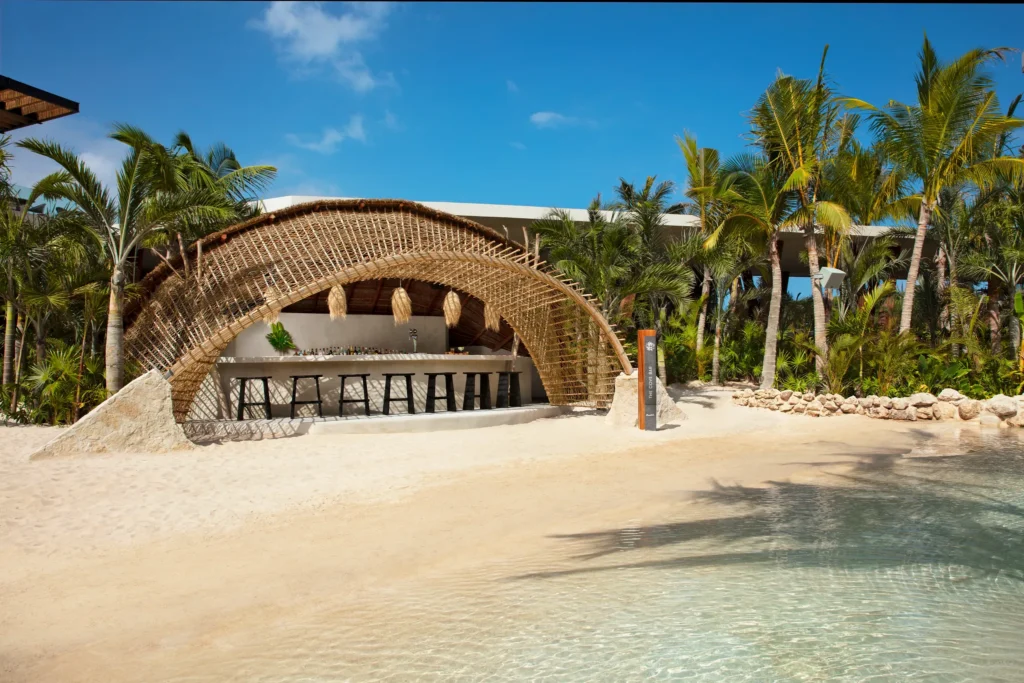 The Cove Bar at Secrets Moxché Playa del Carmen featuring a tropical beach pool bar with a curved bamboo canopy beside a lagoon-style pool.