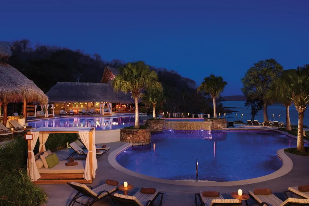 Panoramic nighttime view of the main pool at Secrets Papagayo Costa Rica illuminated with tropical lighting and ocean views.