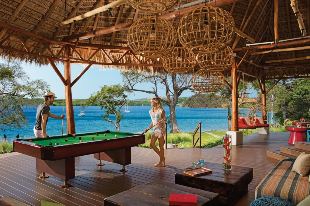 Sugar Reef Beach and Pool Bar at Secrets Papagayo Costa Rica featuring an open-air tropical bar with thatched roof, pool table, lounge seating, and panoramic ocean views.