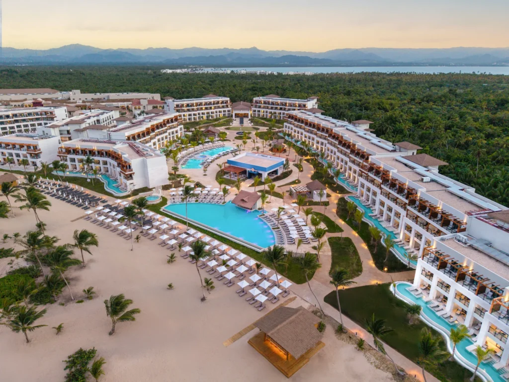 Sunset aerial view of Secrets Playa Esmeralda Resort & Spa with glowing lights and tropical scenery.
