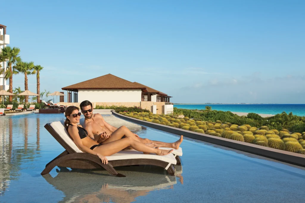 Couple relaxing on in-water loungers at the infinity pool with ocean views at Secrets Playa Mujeres Golf & Spa Resort.