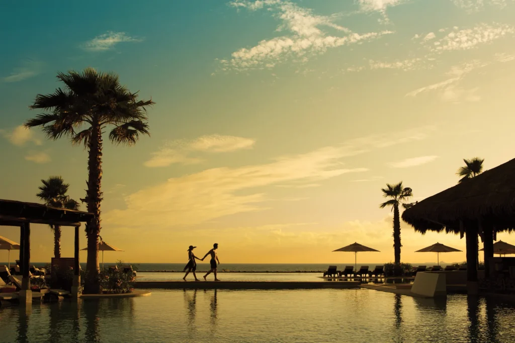 Couple walking across a pool bridge at sunset overlooking the Caribbean Sea at Secrets Playa Mujeres Golf & Spa Resort in Cancun.