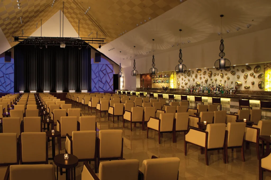 Showtime Theater Bar at Secrets Playa Mujeres Golf & Spa Resort featuring a stage for nightly entertainment, lounge seating, and a full-service cocktail bar.