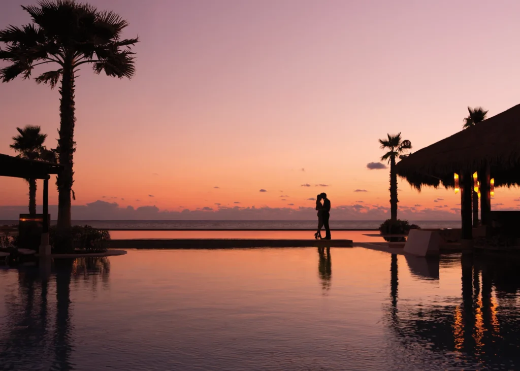 Silhouette of a couple kissing at sunset by the infinity pool at Secrets Playa Mujeres Golf & Spa Resort.