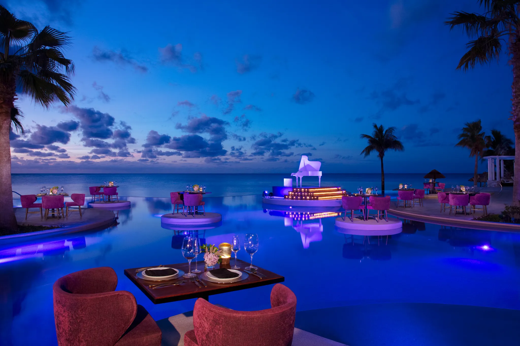 Romantic candlelit dinner setup on platforms over the infinity pool at Secrets Riviera Cancun Resort & Spa at sunset.