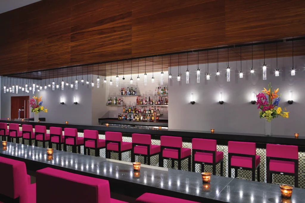 Showstopper Theater Bar at Secrets Riviera Cancun featuring vibrant pink bar stools, modern lighting, and premium cocktails during live entertainment.