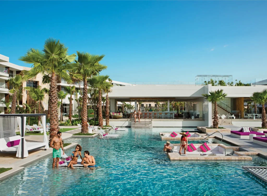 The Bar at Secrets Riviera Cancun overlooking the Energy Pool with swim-up seating and tropical palm surroundings.
